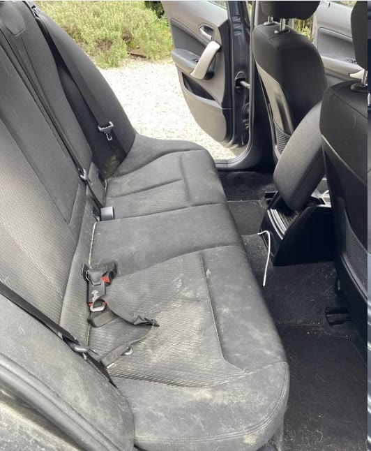 Sedili posteriori di un'auto in tessuto scuro coperti da polvere chiara e aloni