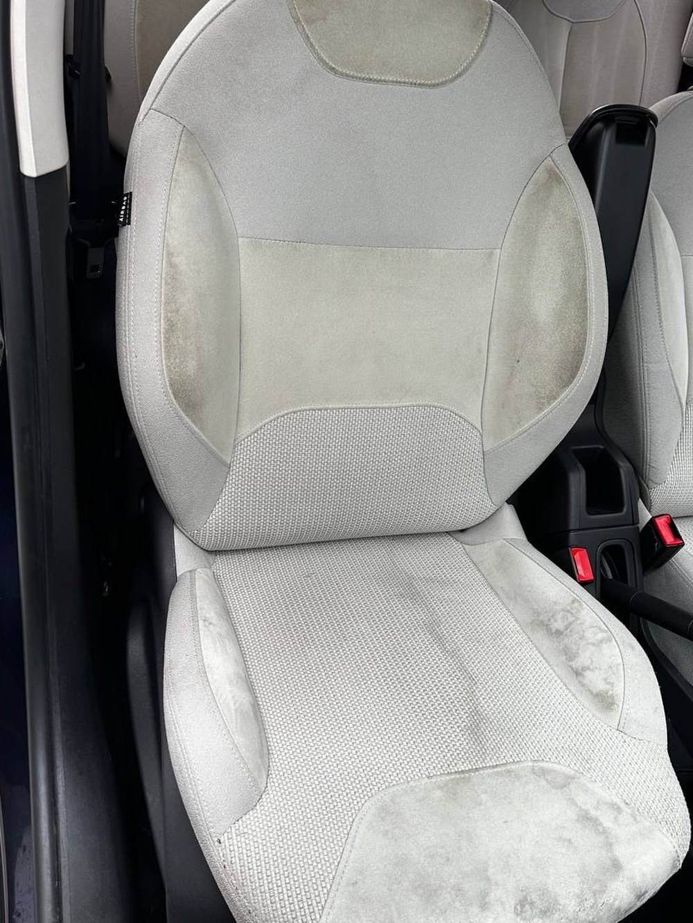 Sedile anteriore di un'auto in tessuto grigio chiaro, con aloni scuri sullo schienale e sulla seduta